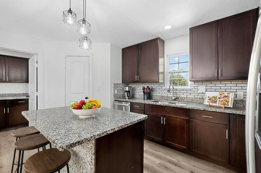 Kitchen featuring dark brown cabinetry, light stone countertops, a kitchen island, light wood finished floors, and recessed lighting