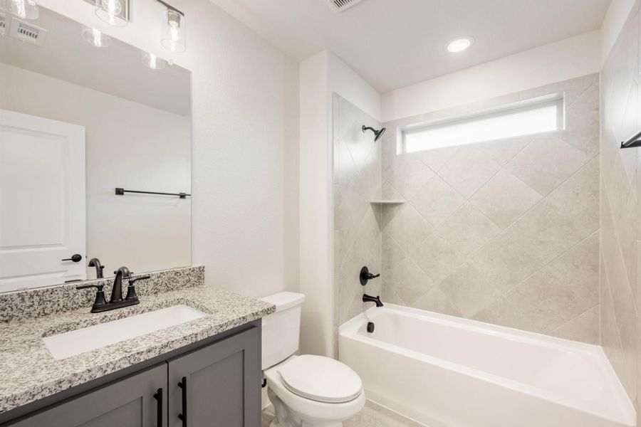 Bathroom with gray vanity, granite countertop, and tiled tub-shower combo with black fixtures