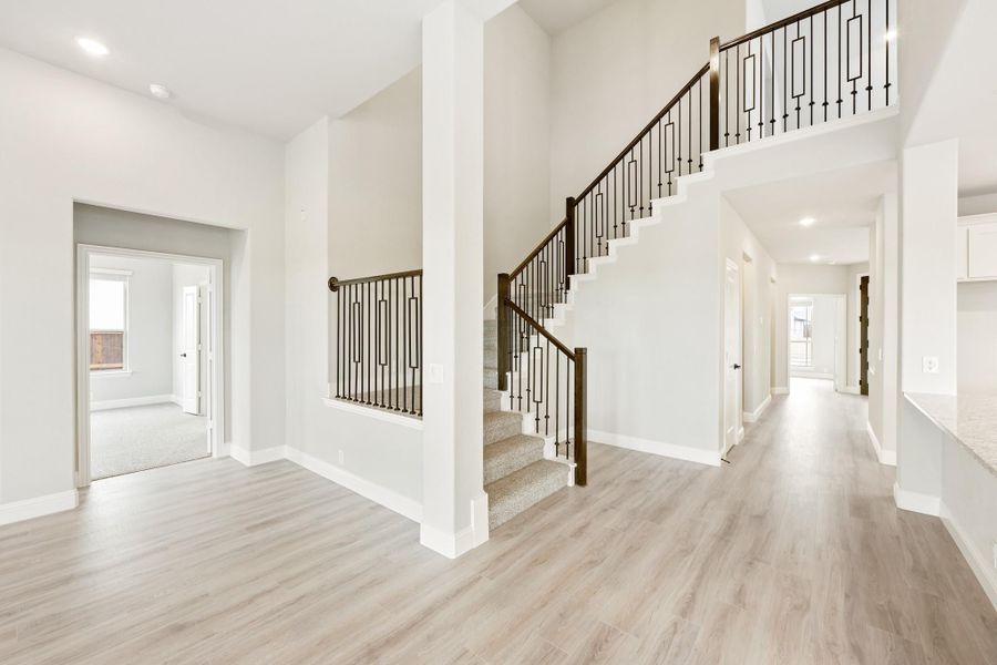 Open foyer with two-story staircase, iron balusters, wood handrail, and light hardwood floors Open foyer with two-story staircase, iron balusters, wood handrail, and light hardwood floors