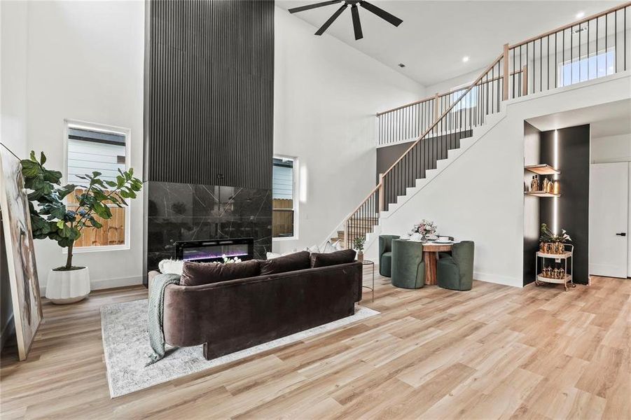 Two-story living area featuring a tall fireplace with a fluted black accent wall and black marble-look surround, light wood-finish flooring, and a contemporary open staircase with metal spindles and wood handrails