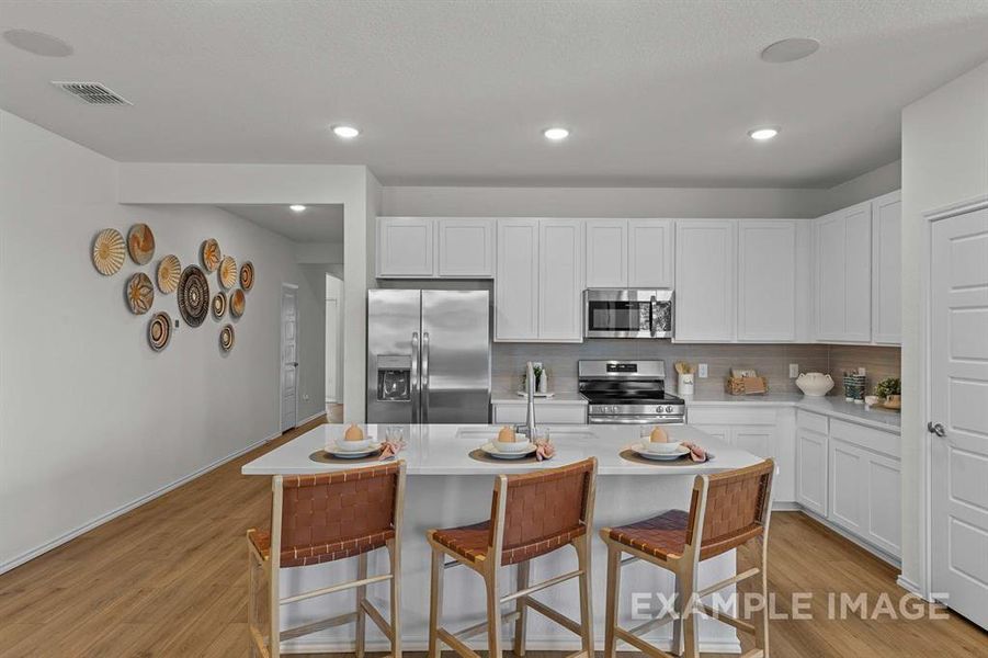 Kitchen featuring backsplash, a breakfast bar, stainless steel appliances, a kitchen island with sink, and white cabinets