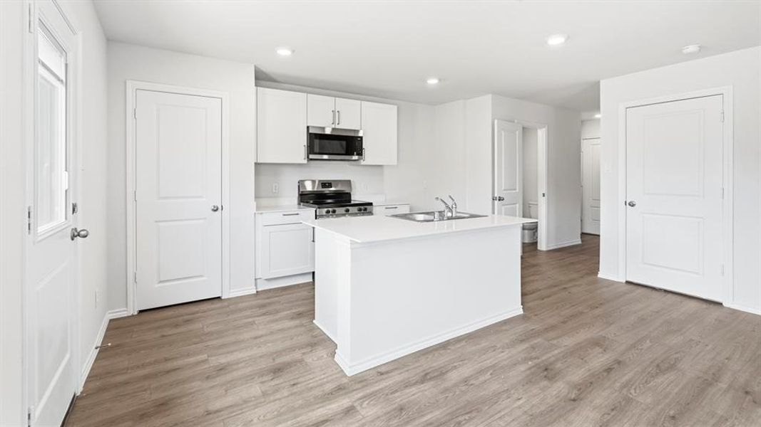 Kitchen with light countertops, stainless steel appliances, a center island with sink, white cabinets, and light wood-style floors