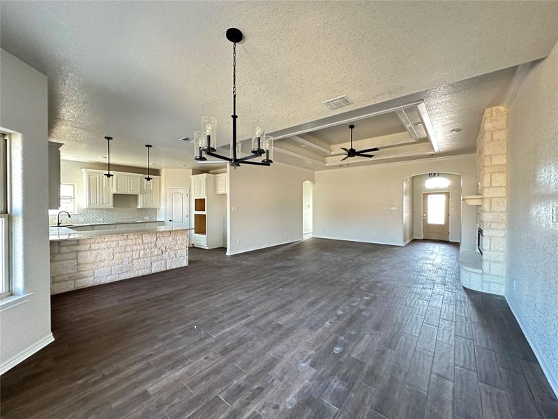 Unfurnished living room featuring a textured ceiling, arched walkways, a raised ceiling, a ceiling fan, and a chandelier