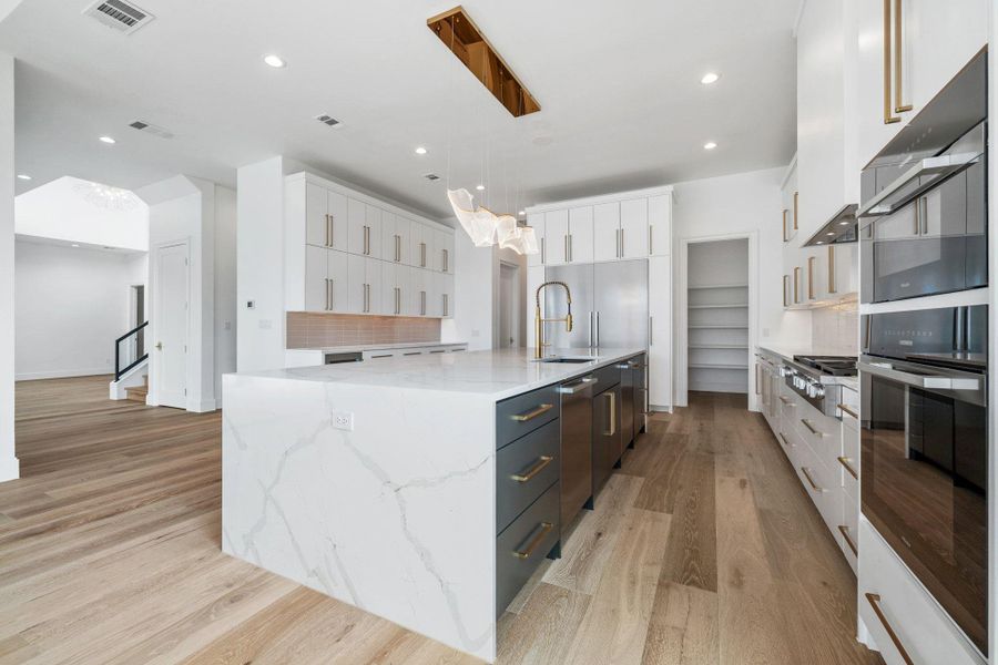 Kitchen featuring dual tone cabinets, stainless steel appliances, light wood-style flooring, pendant lighting, and light stone countertops