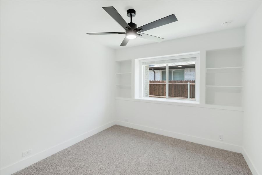 Empty bedroom with carpet, ceiling fan, built-in shelves flanking a window with backyard view Empty bedroom with carpet, ceiling fan, built-in shelves flanking a window with backyard view