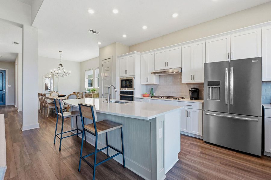 Kitchen featuring stainless steel appliances, white cabinetry, a kitchen bar, backsplash, and dark wood-style flooring Kitchen featuring stainless steel appliances, white cabinetry, a kitchen bar, backsplash, and dark wood-style flooring