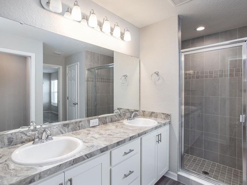 Dual vanity en-suite bath with a decorative tiled shower with glass enclosure - Photo showcases a home with similar finishes. Colors and design options in actual home for sale may differ.