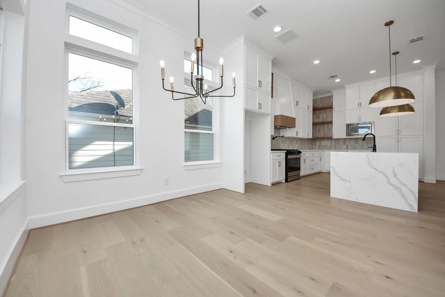 A bright, modern kitchen and dining space featuring crisp white cabinetry, marble countertops, and warm wood flooring. Thoughtful pendant lighting, expansive windows, and ample storage create a functional yet inviting atmosphere.