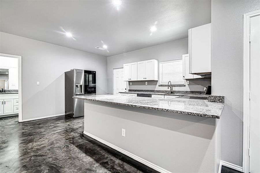 Kitchen with range, stainless steel refrigerator with ice dispenser, light stone counters, and white cabinets