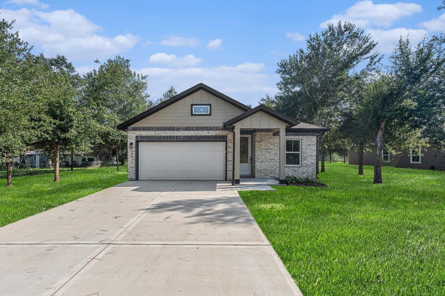 This photo features a charming single-story home with a modern exterior. It has a clean, paved driveway leading to a two-car garage. The house is surrounded by a lush green lawn and mature trees, creating a serene and inviting atmosphere.