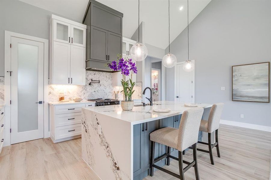Kitchen with a breakfast bar, light wood-type flooring, decorative backsplash, pendant lighting, and high vaulted ceiling