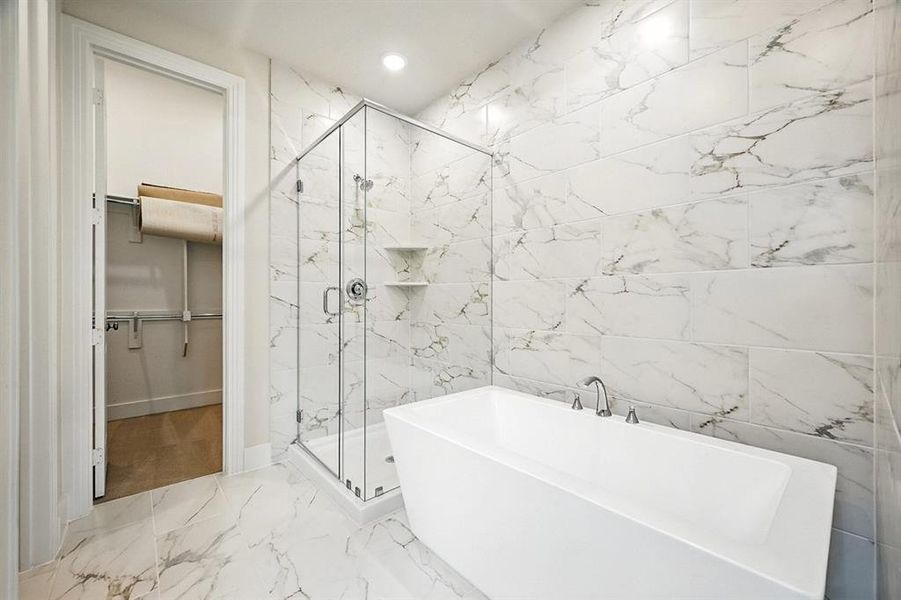 Full bathroom featuring a spacious closet, a marble finish shower, light marble finish flooring, a soaking tub, and tile walls Full bathroom featuring a spacious closet, a marble finish shower, light marble finish flooring, a soaking tub, and tile walls