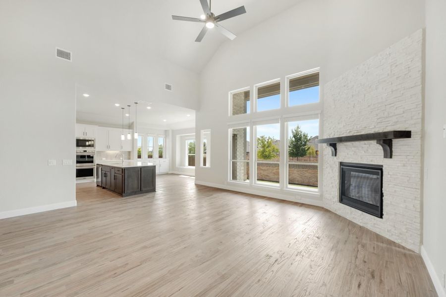 Open living area with vaulted ceiling, stone fireplace, hardwood floors, and open kitchen with dark island. Open living area with vaulted ceiling, stone fireplace, hardwood floors, and open kitchen with dark island.