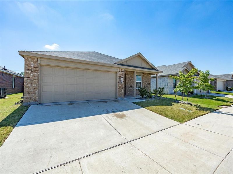 Front exterior featuring a tan brick facade, an attached garage, a concrete driveway, and mature landscaping