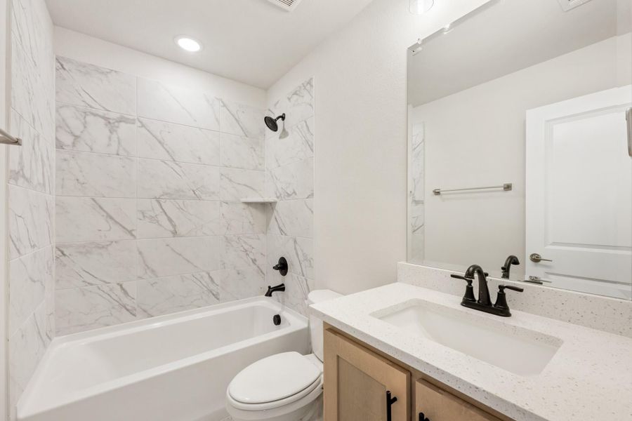 Bathroom with marble-tile tub surround, white quartz vanity, and black fixtures