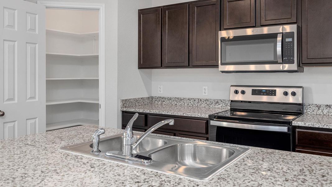 Kitchen with dark wood finish cabinetry, stainless steel appliances, and light stone counters