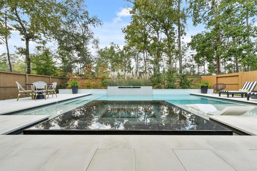 360 negative edge spa with black pebbletec, sheer decent water feature on tile wall.