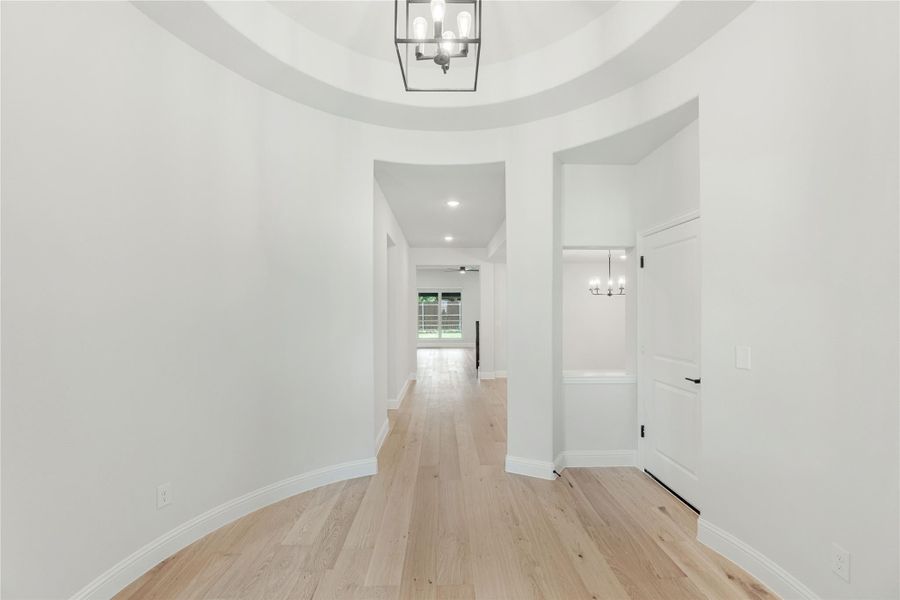 Circular foyer with tray ceiling, pendant light fixture, and light hardwood floors leading to hallway