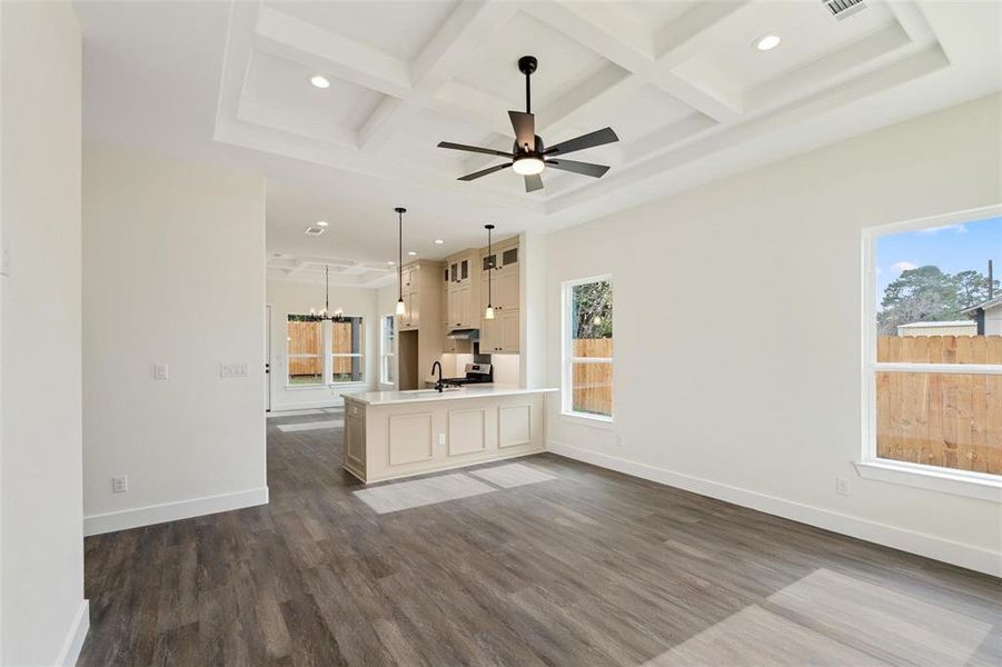 Unfurnished living room with coffered ceiling, dark wood-type flooring, a chandelier, and a ceiling fan