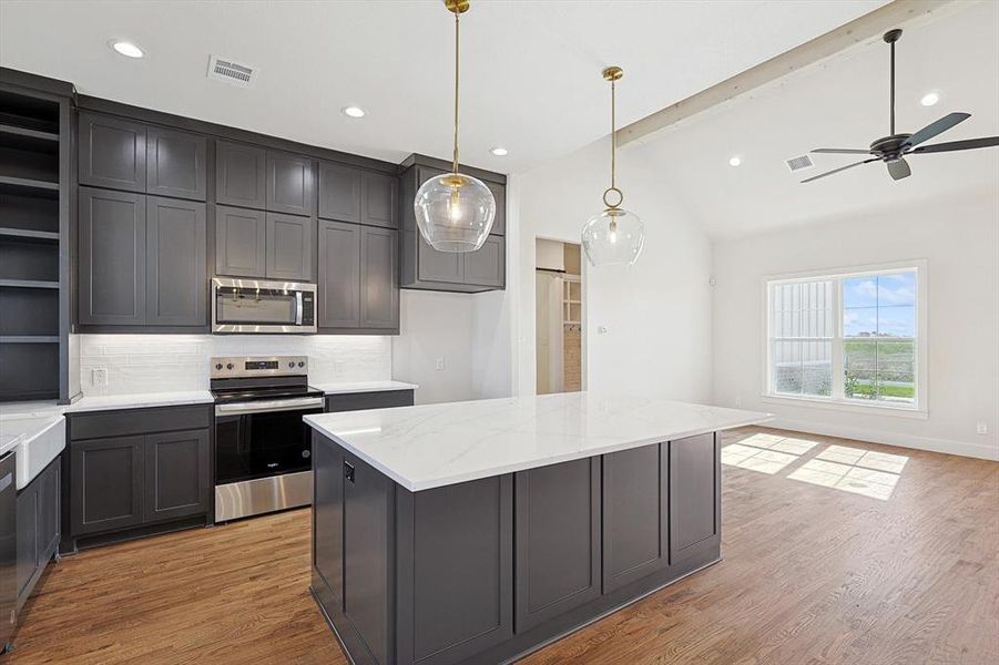 Kitchen featuring appliances with stainless steel finishes, a center island, lofted ceiling with beams, and decorative light fixtures