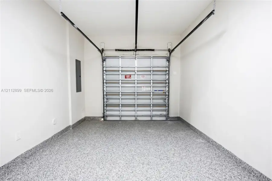 Enclosed garage space featuring a metal overhead door, seamless speckled epoxy flooring, and crisp white wall finishes