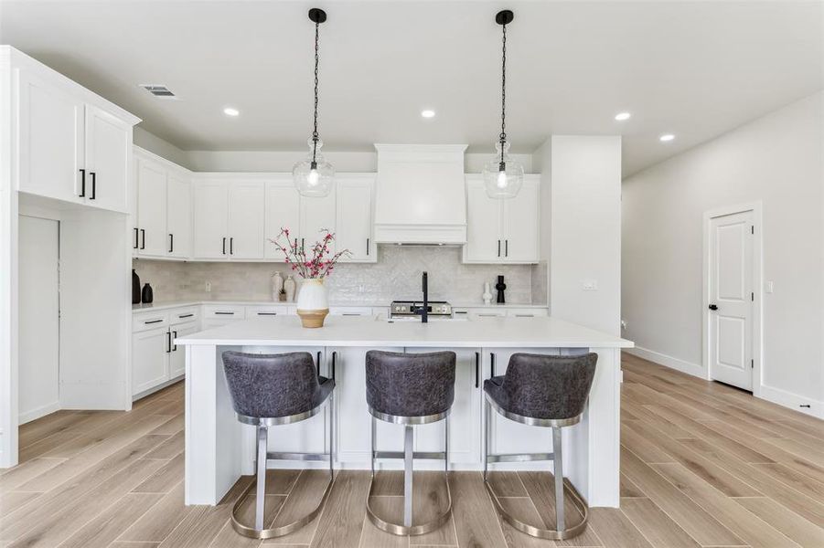 Kitchen with custom exhaust hood, tasteful backsplash, light hardwood / wood-style flooring, and white cabinetry