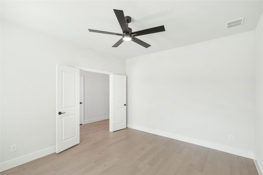 Empty bedroom with light wood floors, black ceiling fan, and open double doors Empty bedroom with light wood floors, black ceiling fan, and open double doors