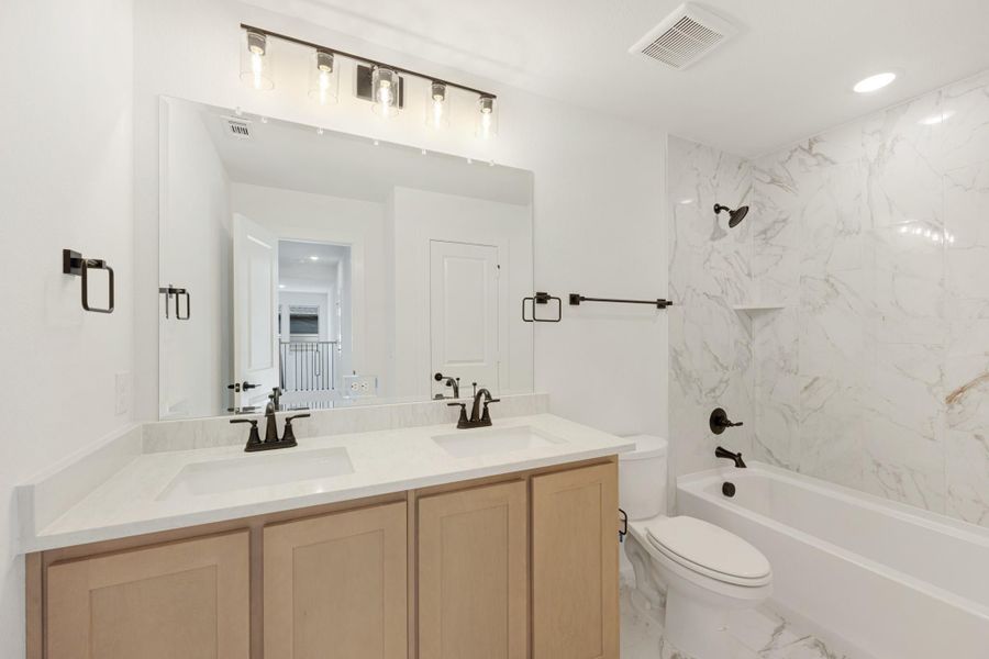 Bathroom with double vanity, wood cabinets, white quartz countertop, and marble-tile tub surround with dark bronze fixtures