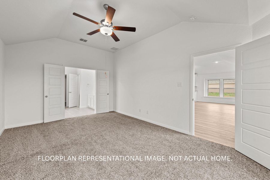 A spacious bedroom presents vaulted ceilings, soft carpet, and a convenient pass-through to a well-appointed bathroom.