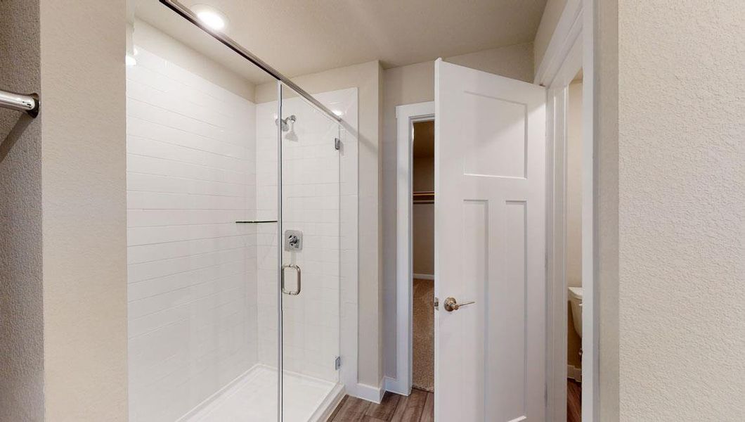 Bathroom with a shower stall, wood finished floors, a spacious closet, and a textured wall