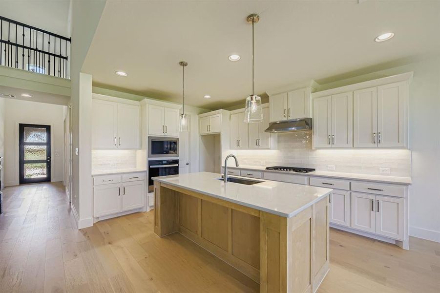 Kitchen with backsplash, recessed lighting, white cabinetry, hanging light fixtures, and a center island with sink
