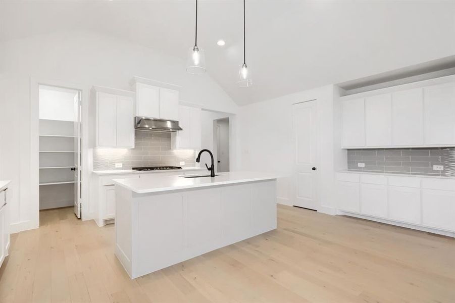 Modern kitchen featuring a central island, light wood-finish flooring, white cabinetry, a subway tile backsplash, and vaulted ceilings
