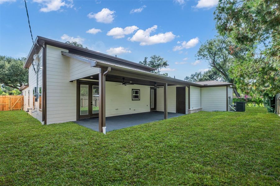 This photo shows the back of a single-story home with a covered patio and a spacious grassy yard, ideal for outdoor activities.