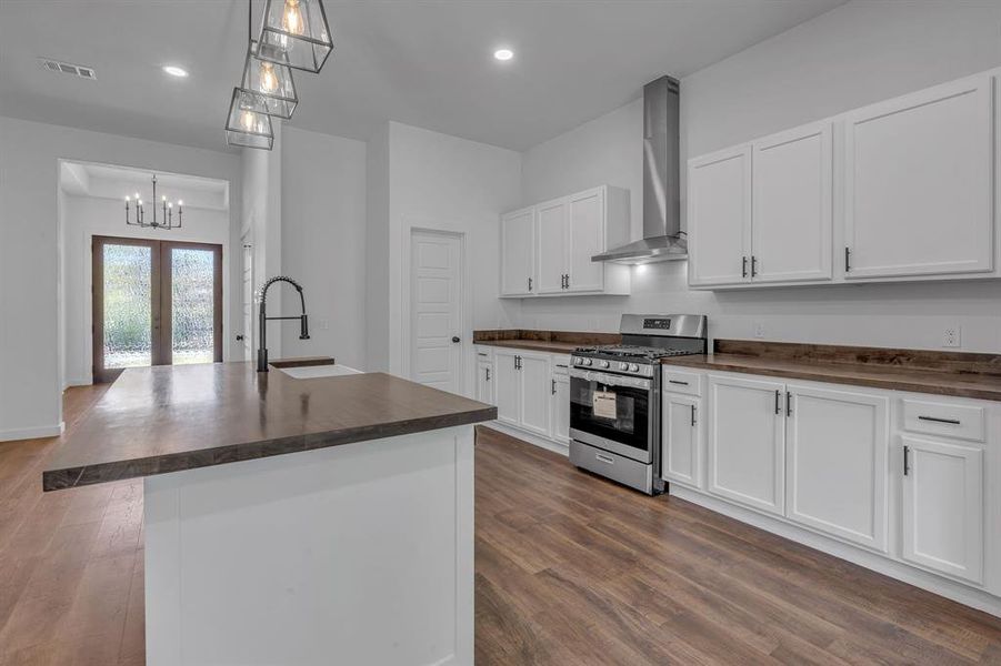 Kitchen with a center island with sink, sink, hanging light fixtures, wall chimney range hood, and stainless steel gas stove