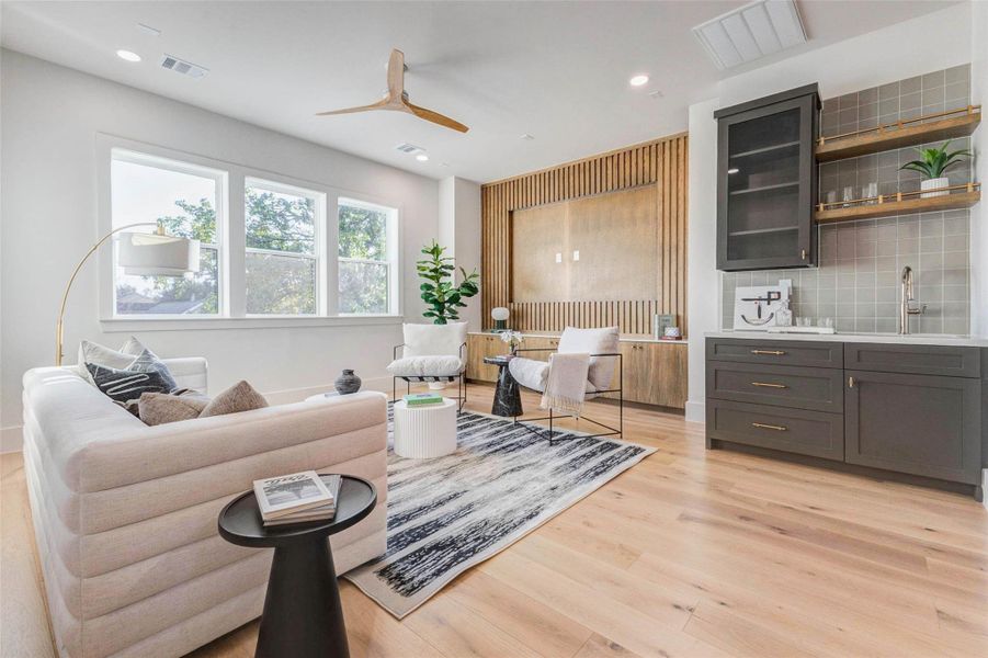 The upstairs game room or media lounge offers wide-plank hardwood floors, a wall-mounted entertainment niche with wood slat accent, and a built-in wet bar featuring floating shelves and glass-front cabinets.