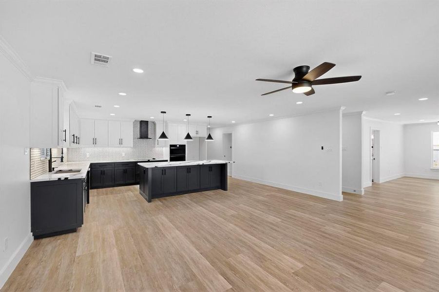 Kitchen with dark cabinetry, decorative backsplash, white cabinets, open floor plan, and hanging light fixtures