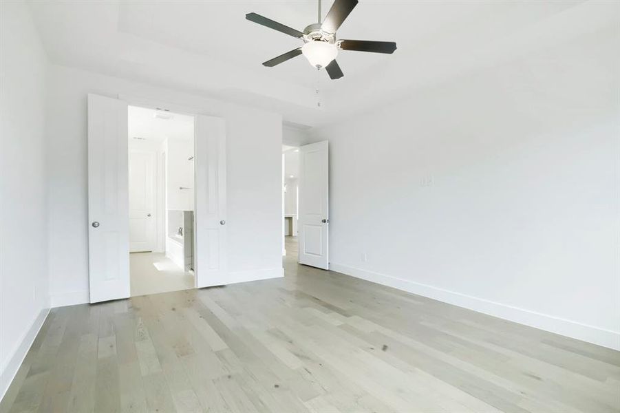 Spacious room featuring light wood-finish flooring, a contemporary ceiling fan with integrated lighting, and a tray ceiling
