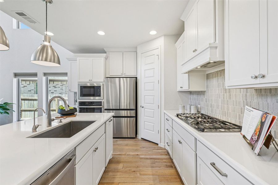 The kitchen features white cabinetry, stainless steel appliances, a gas cooktop, and a spacious island with a sink