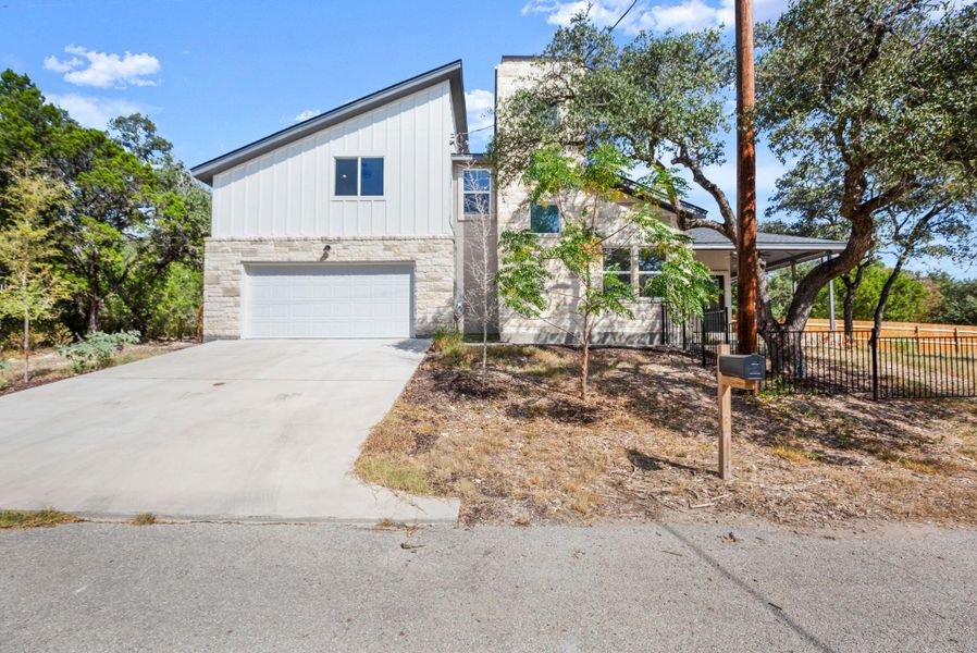 View of front facade featuring board and batten siding, stone siding, an attached garage, and driveway