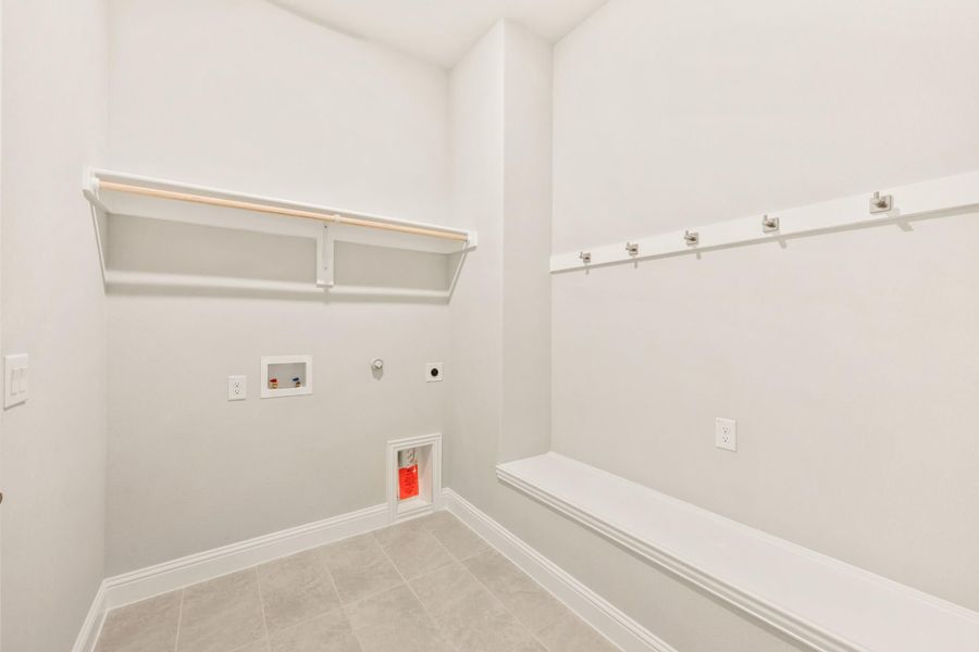 Laundry and mudroom area with white walls, built-in shelf, coat hooks, and bench seating on tile floor Laundry and mudroom area with white walls, built-in shelf, coat hooks, and bench seating on tile floor