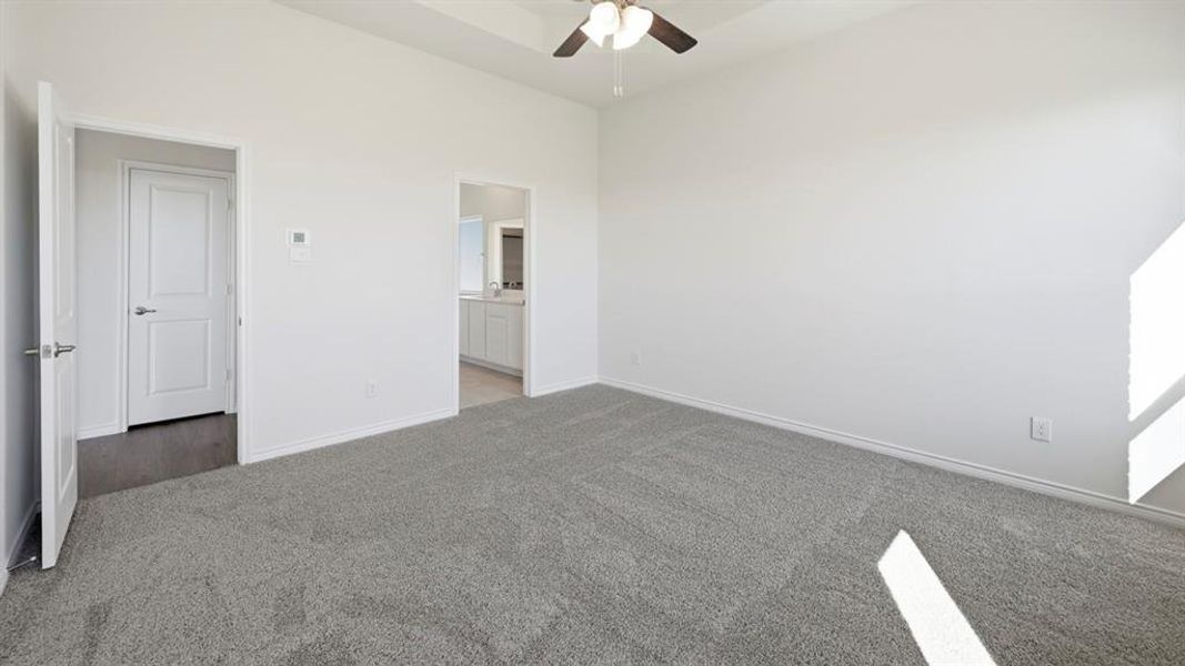 Carpeted room featuring a ceiling fan, a white paneled door, and an entryway leading to a bathroom with a white vanity