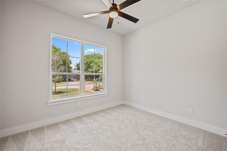 Bright interior room featuring a large window with white trim, light gray carpet, and a ceiling fan with integrated lighting