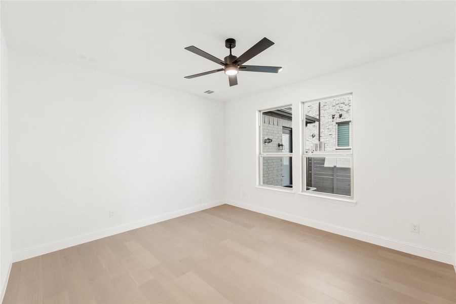 Empty bedroom with light hardwood floors, ceiling fan, and double windows with exterior view