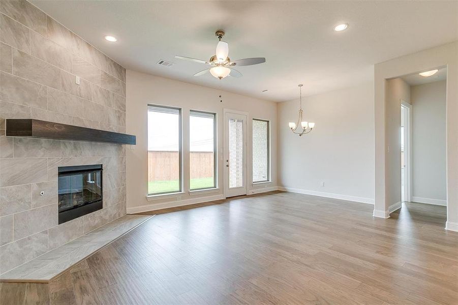 Unfurnished living room featuring ceiling fan with notable chandelier, a tiled fireplace, light wood-type flooring, and tile walls