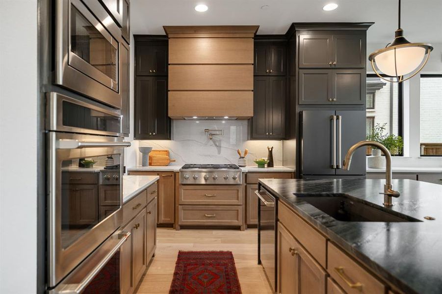 Kitchen featuring dark stone counters, light wood-type flooring, stainless steel appliances, pendant lighting, and backsplash Kitchen featuring dark stone counters, light wood-type flooring, stainless steel appliances, pendant lighting, and backsplash