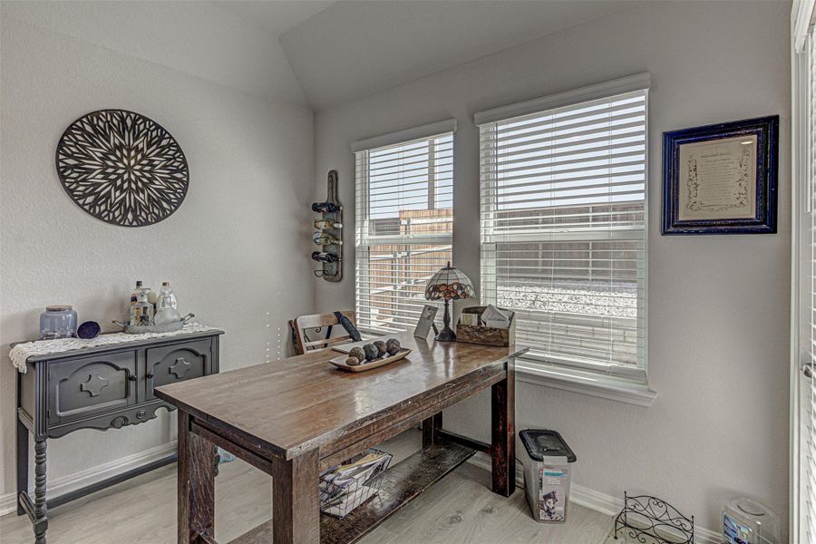 Office area with light wood finished floors, lofted ceiling, and a textured wall