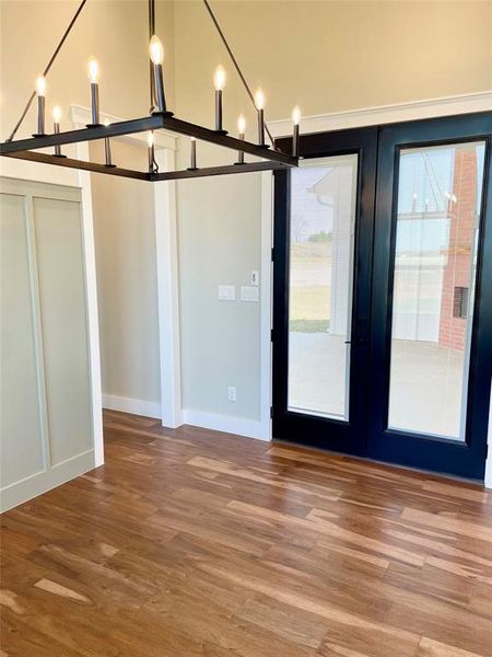 Unfurnished dining area featuring dark wood-style flooring, hanging lights, and french doors
