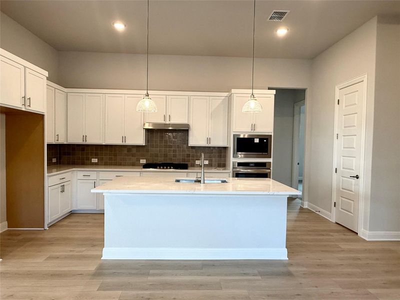 Kitchen with appliances with stainless steel finishes, tasteful backsplash, white cabinets, a center island with sink, and pendant lighting Kitchen with appliances with stainless steel finishes, tasteful backsplash, white cabinets, a center island with sink, and pendant lighting