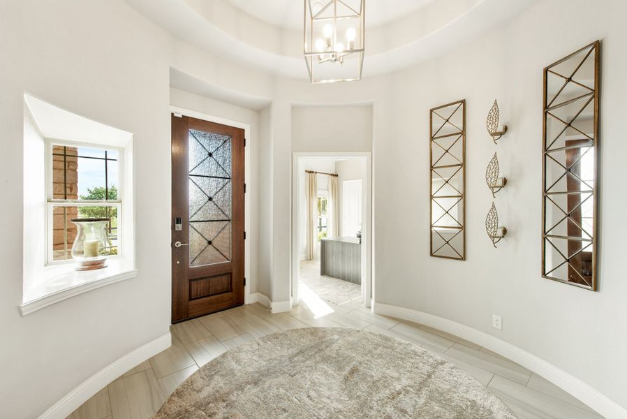 Rounded entryway with wood and glass front door, pendant chandelier, and decorative wall mirrors