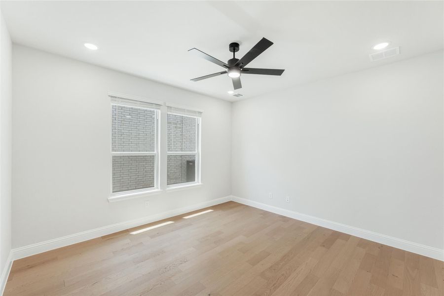 Empty room with light hardwood floors, white walls, black ceiling fan, and a double window